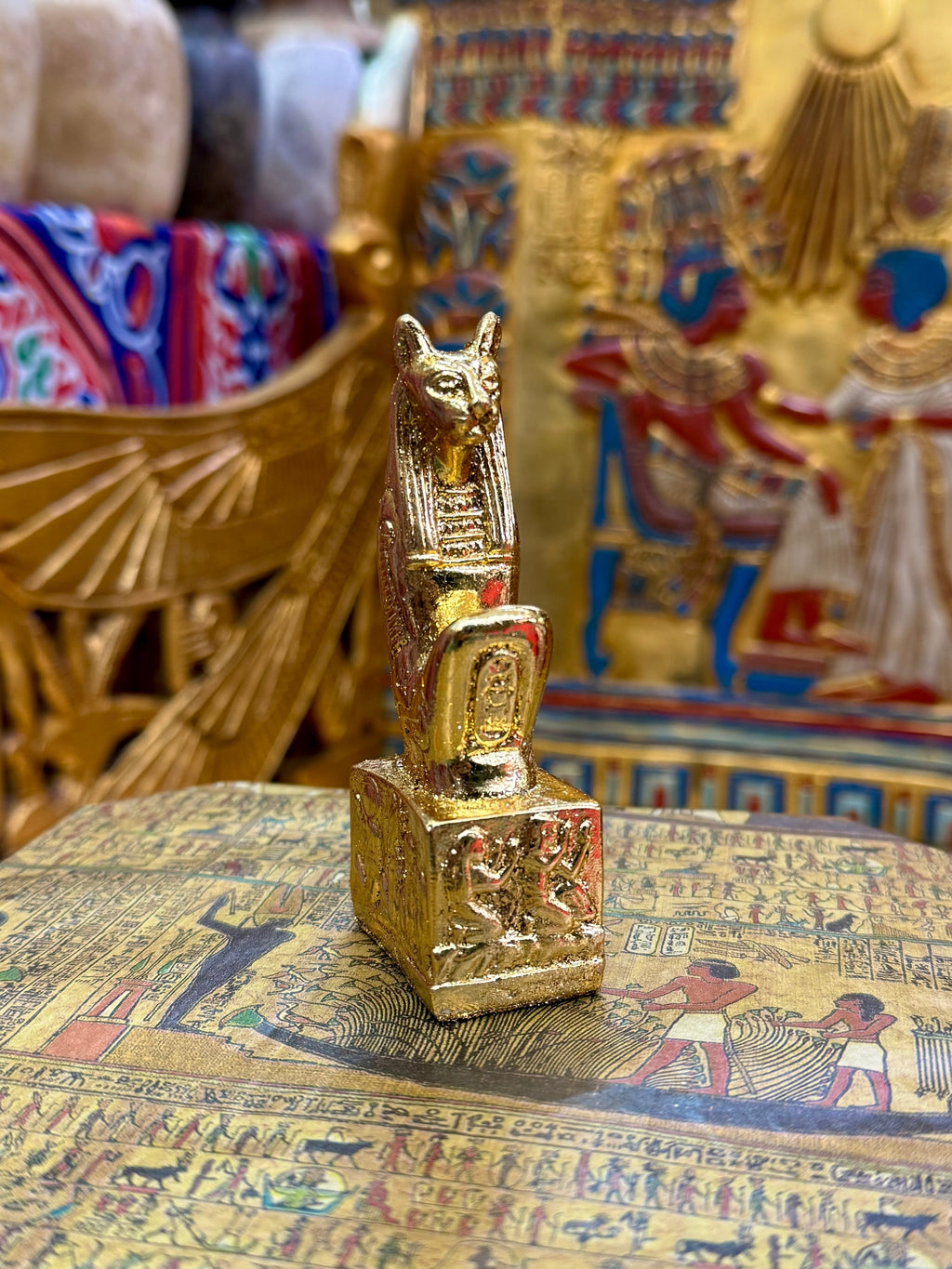 Front angled view of the gold finish Bastet kneeling statue with cat head, pointed ears and decorated square base.