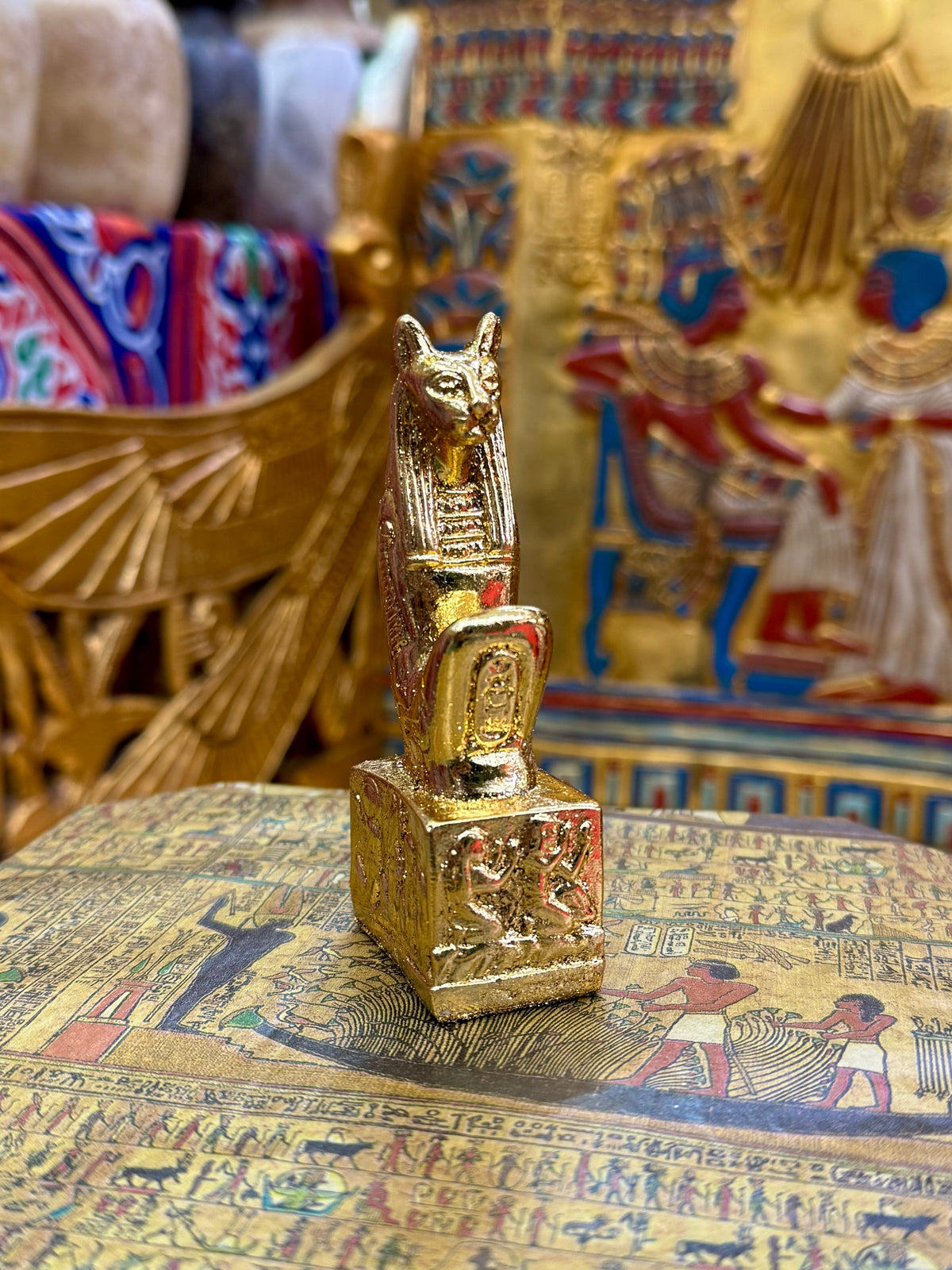 Front angled view of the gold finish Bastet kneeling statue with cat head, pointed ears and decorated square base.