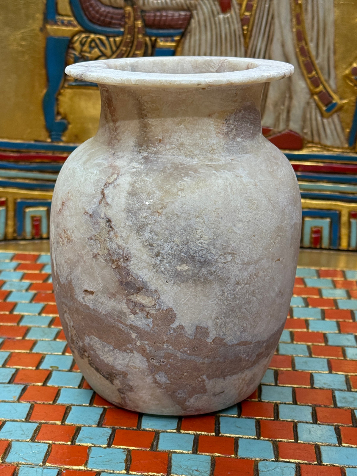 Rounded alabaster vase with a sweeping brown vein, narrow neck and flared rim — unlit full view.