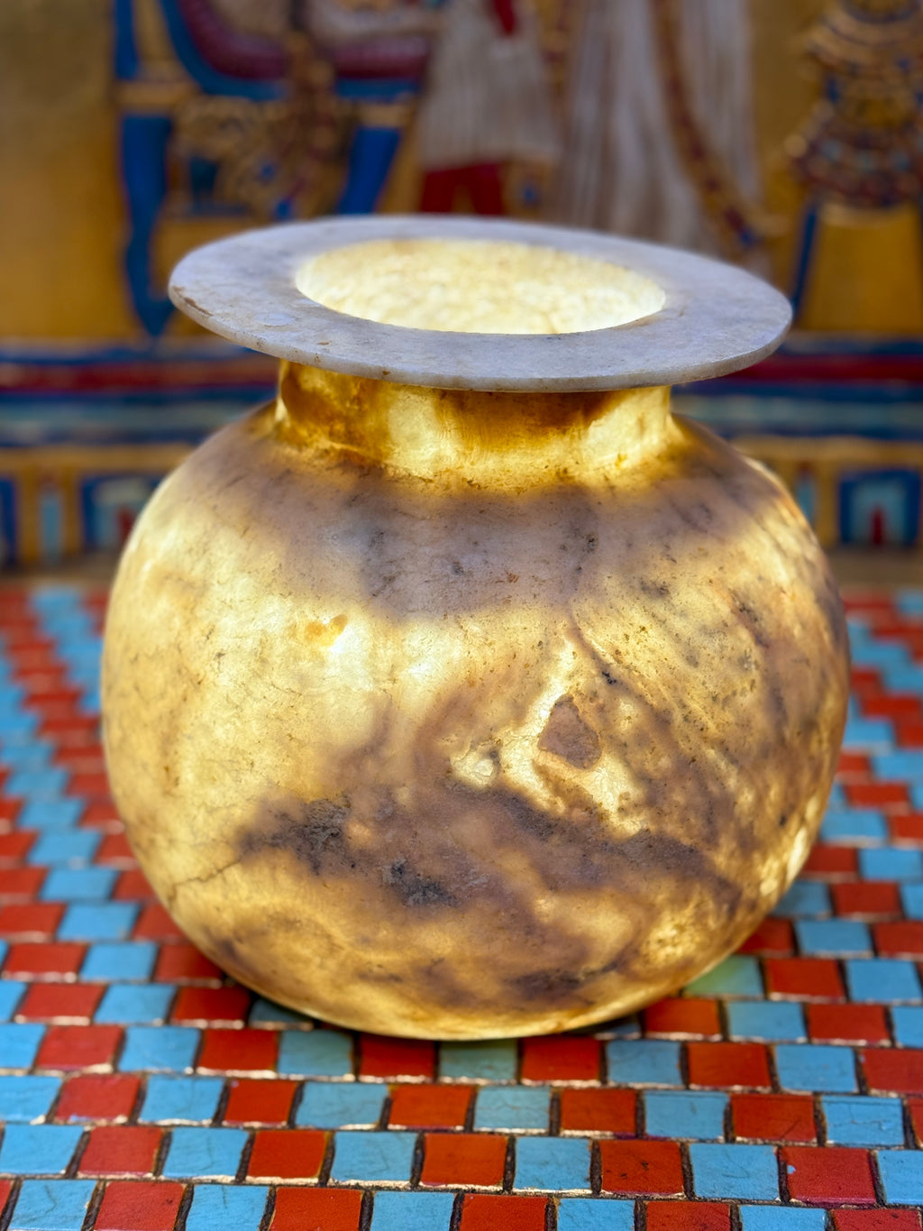 Rounded taupe and cream alabaster vase with sweeping markings, a short neck and wide flat rim — illuminated view.