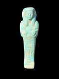 Front of turquoise-coloured stone shabti with a long headdress, crossed arms, incised markings and pale cream patches.