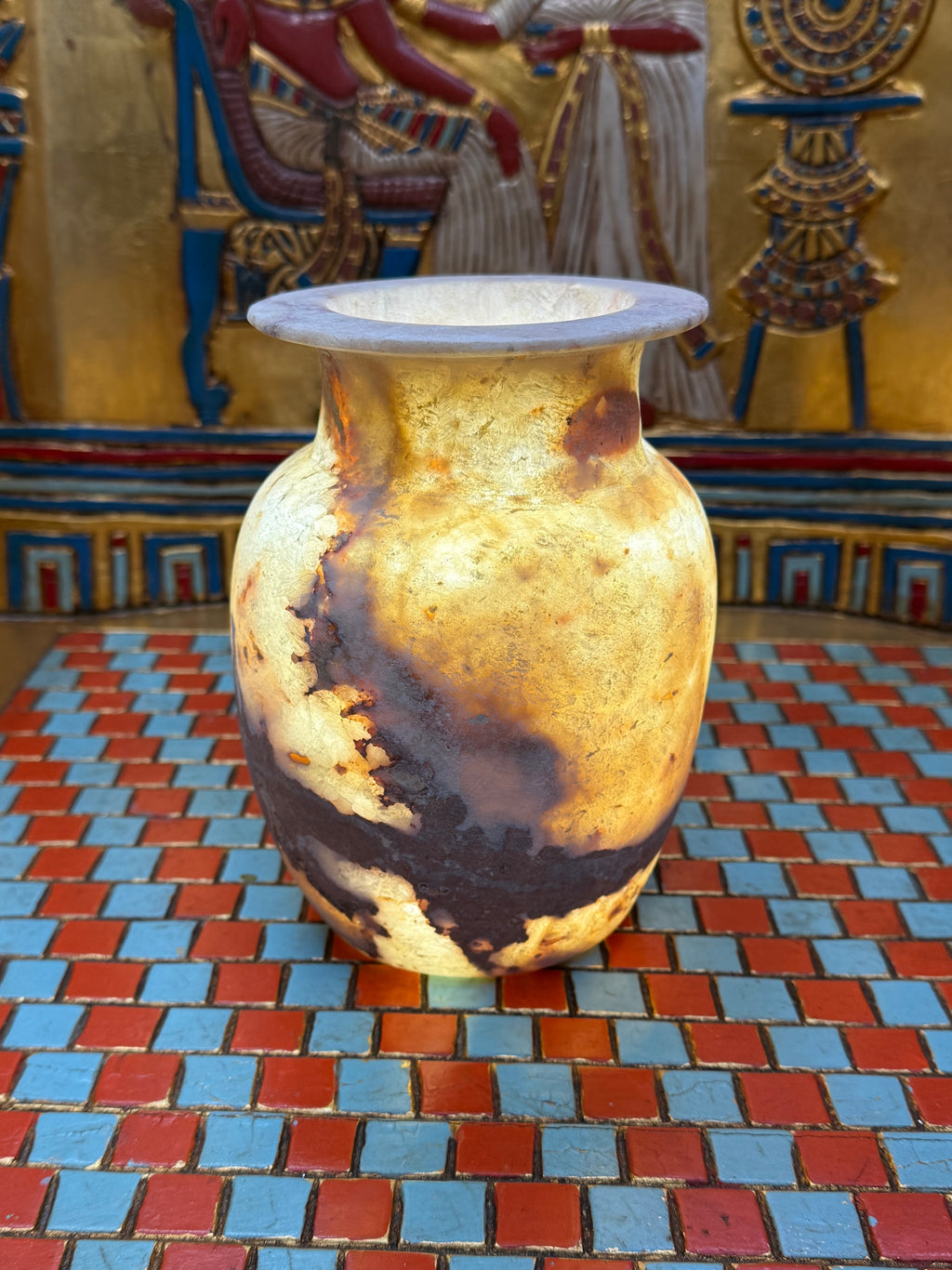 Rounded alabaster vase with a sweeping brown vein, narrow neck and flared rim — illuminated view.
