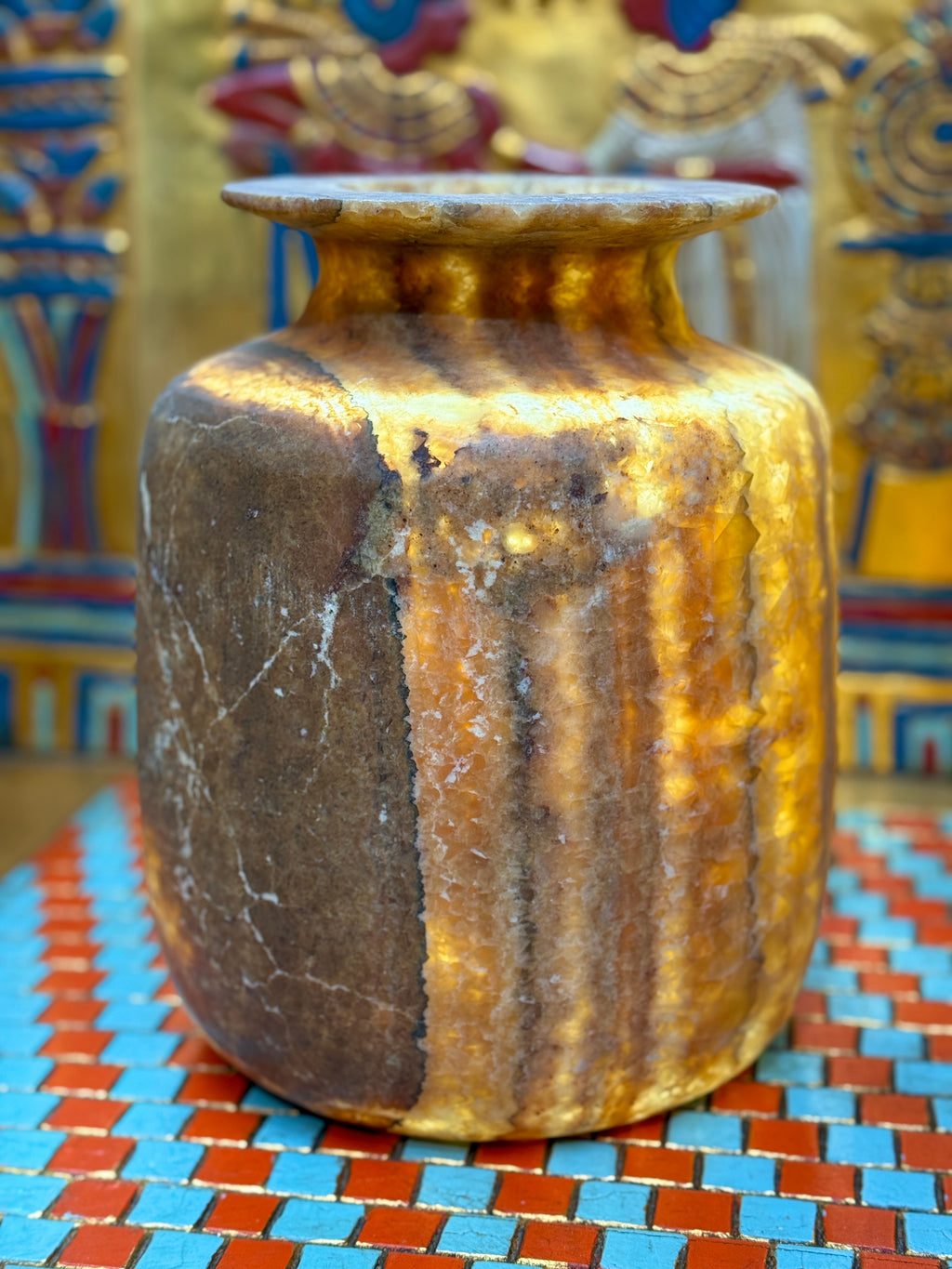 Squared alabaster vase with rounded corners, smoky brown stone, lighter vertical stripes and a flared rim — illuminated view showing amber-coloured stone.