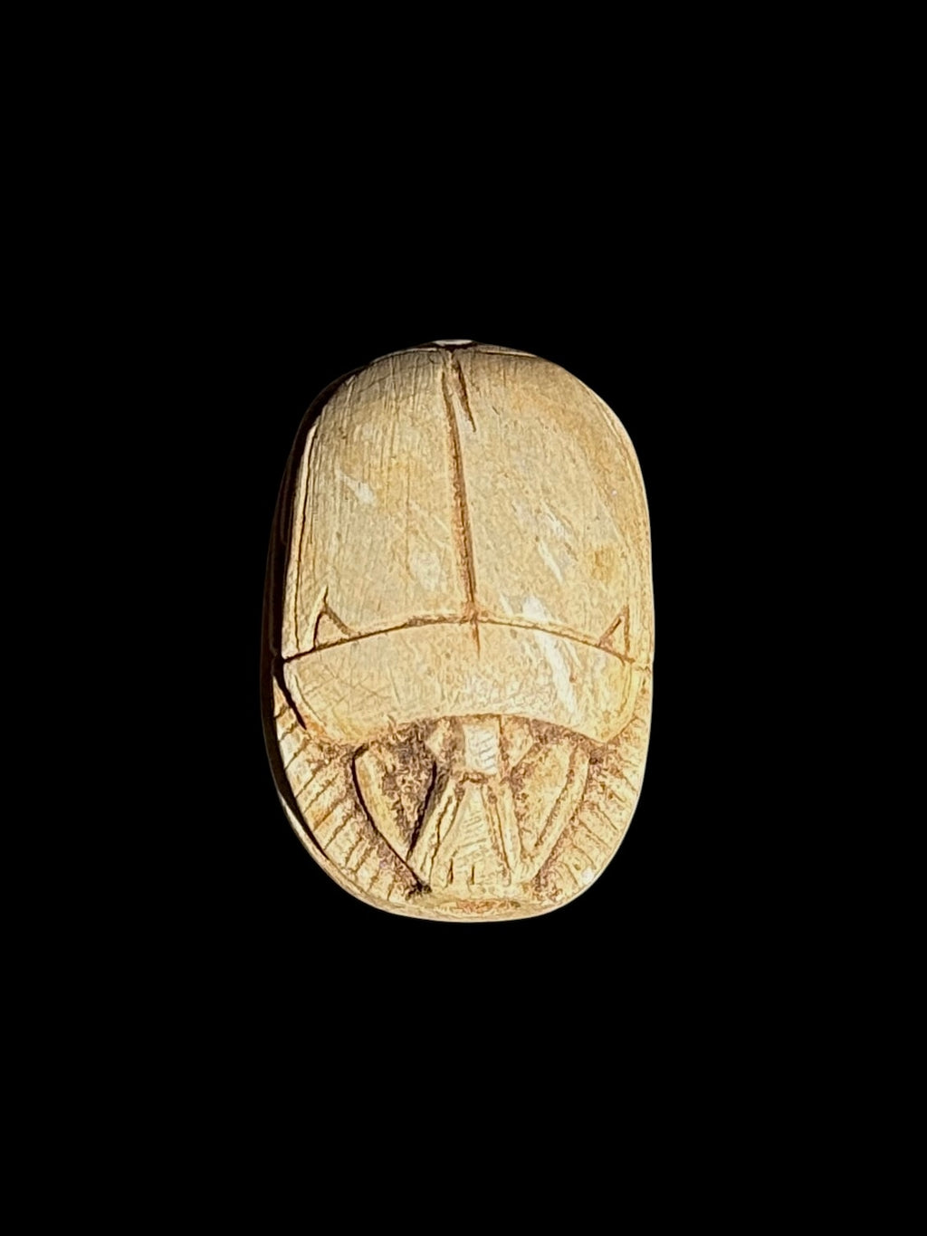 Upper view of a cream and sandy beige stone scarab with incised wing divisions and head details against a black background.