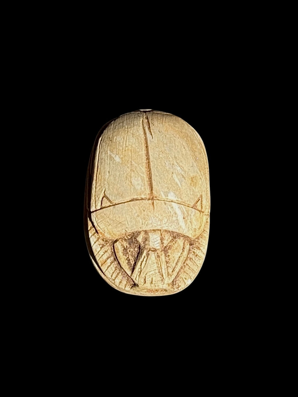 Upper view of a cream and sandy beige stone scarab with incised wing divisions and head details against a black background.