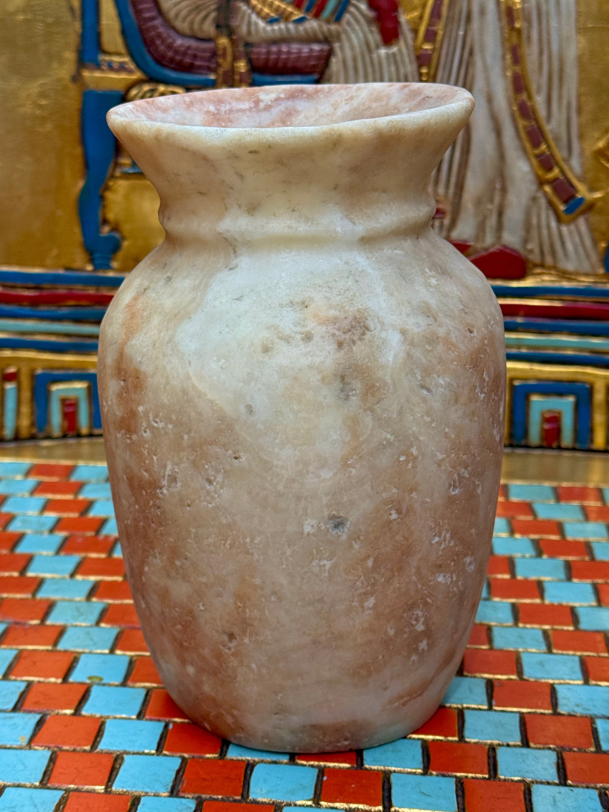 Small curved alabaster vase with cream and taupe markings and a softly flared cup-shaped rim — unlit full view.
