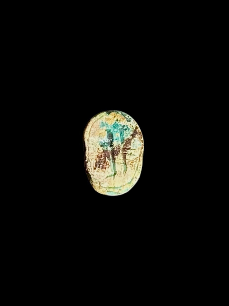 Underside of the stone scarab showing a bordered oval design with figure-like markings in cream, turquoise and brown on a black background.