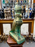 Three-quarter front view of the green and gold Horus falcon statue with a tall crown, folded wings and rectangular base.