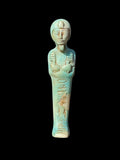 Front view of a turquoise-coloured shabti figurine with crossed arms, headdress, beard and incised markings, with cream and tan surface patches.