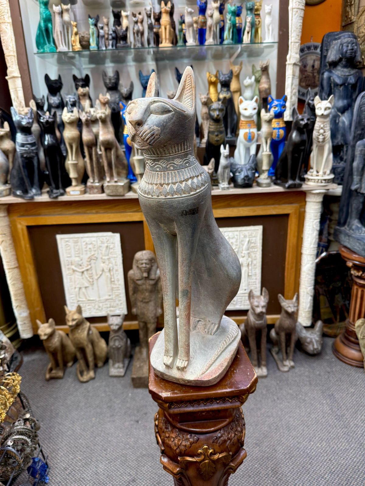 Three-quarter front view of a grey Bastet cat statue with upright ears, patterned collar, long forelegs and rounded base.