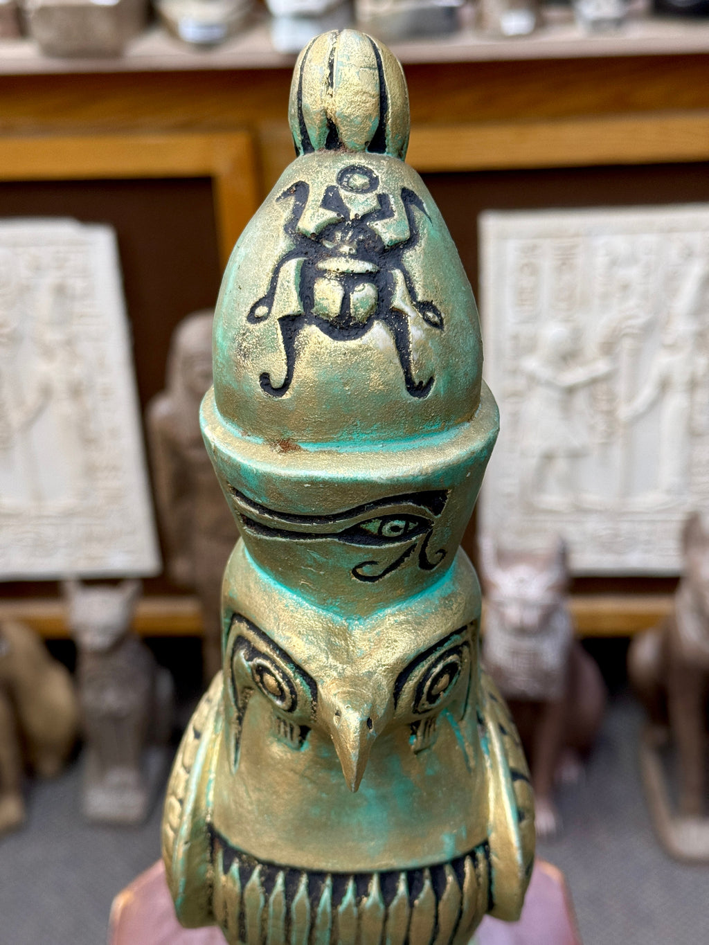 Front close-up of the Horus statue’s crown and face, showing the black scarab and eye motifs above the falcon’s pointed beak.