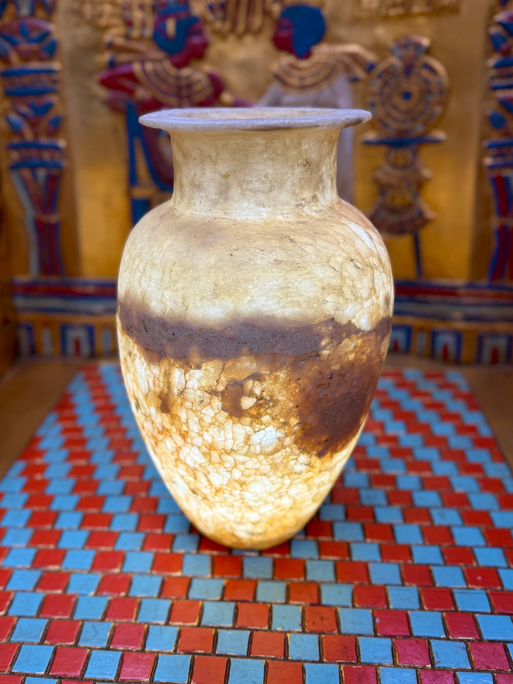 Alabaster vase with a pale upper body, broad earthy band, rounded shoulders and flared neck — illuminated view.