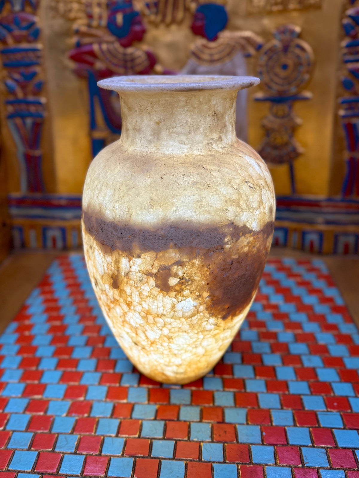 Alabaster vase with a pale upper body, broad earthy band, rounded shoulders and flared neck — illuminated view.