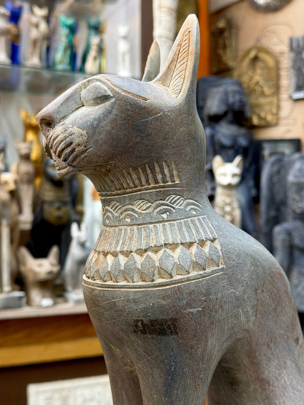 Angled close-up of the Bastet statue's face and collar, with pale incised details and a dark patch on the chest.