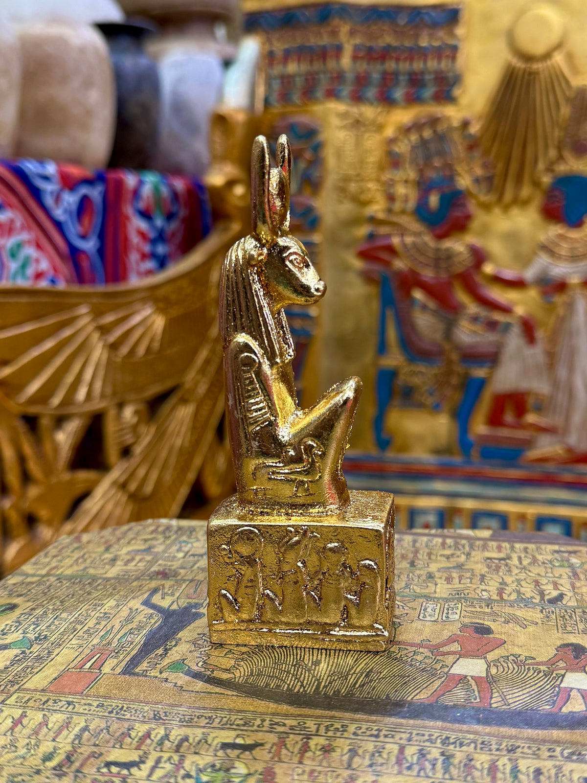 Side view of the gold finish Hathor kneeling statue with horns, sun-disc headdress and decorated square base.