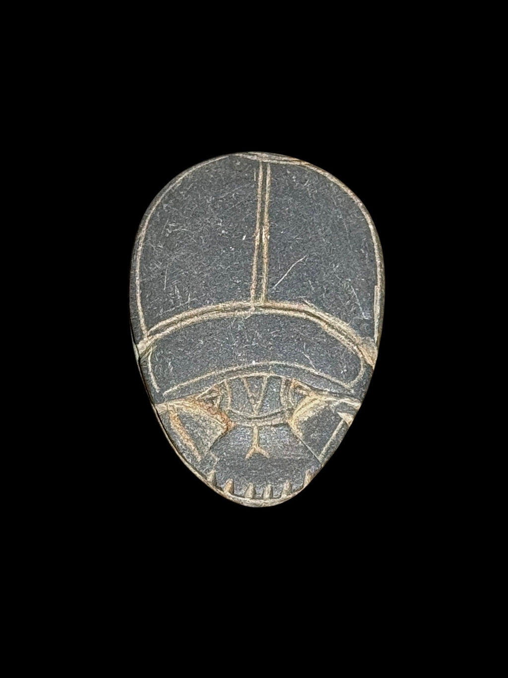 Dark grey stone scarab viewed from above, with pale incised lines outlining the wing cases and head against a black background.