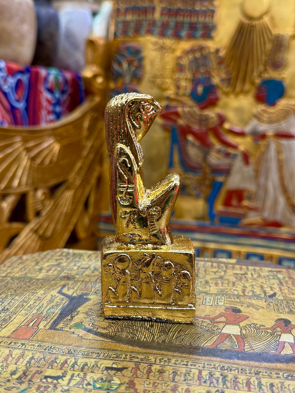 Side view of the gold finish Horus kneeling statue with falcon head and decorated square base.