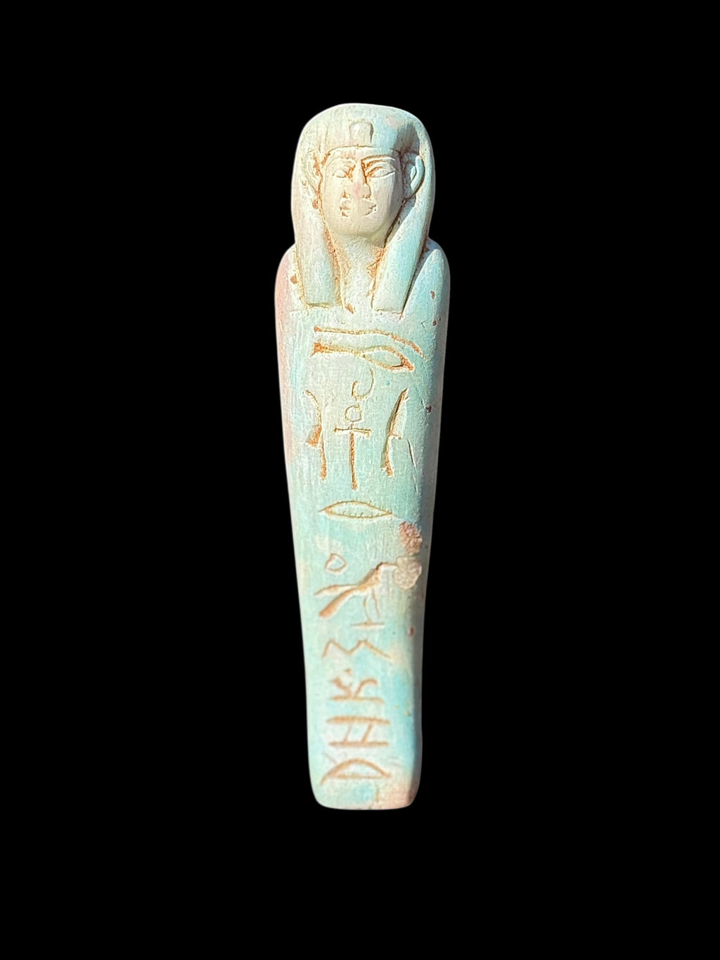 Front view of an elongated shabti figurine with a pale turquoise and cream finish, long headdress and recessed markings accented in tan.