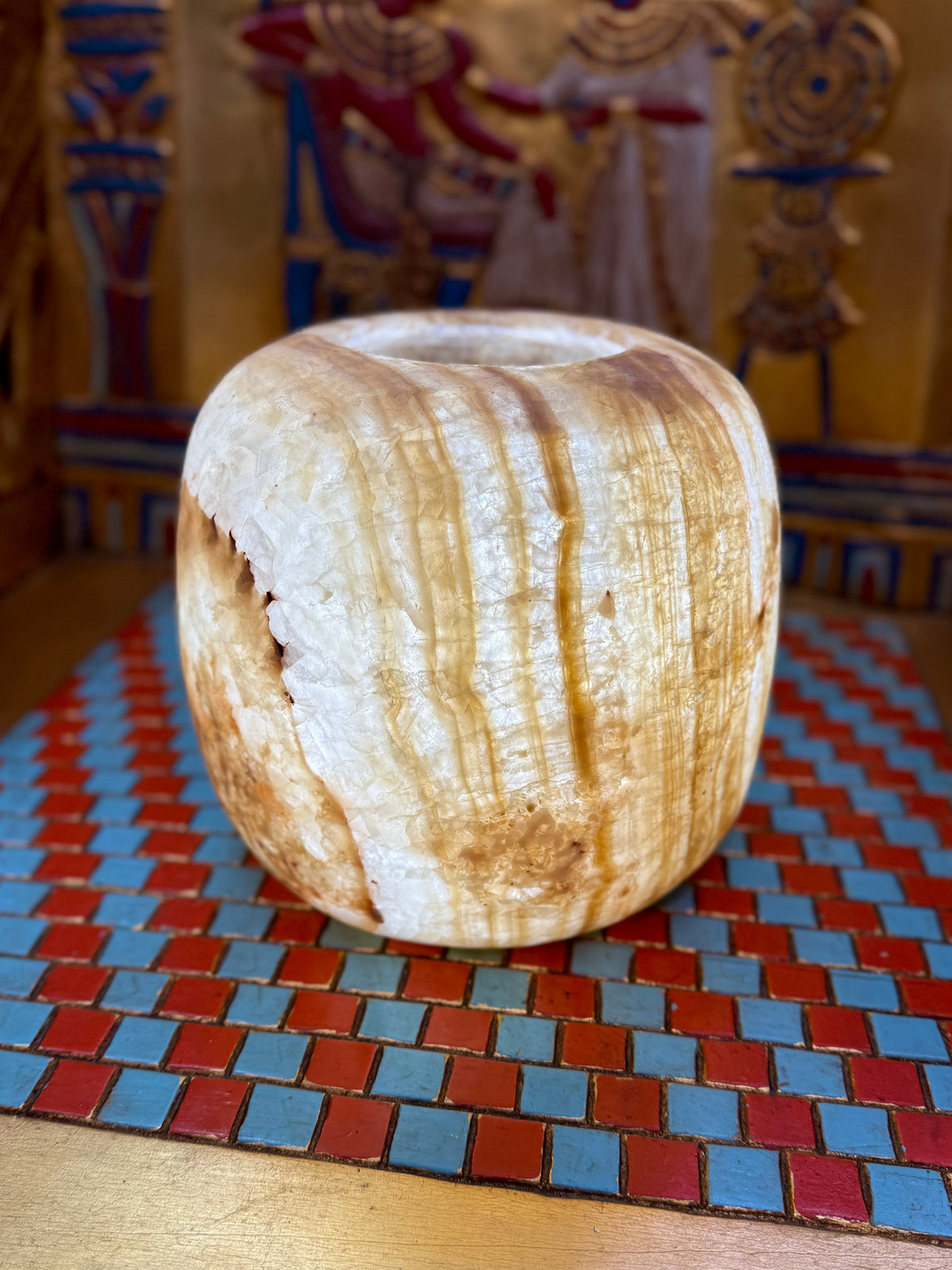 Broad cream alabaster vase with rounded shoulders, golden-brown vertical bands and a simple opening — illuminated view.