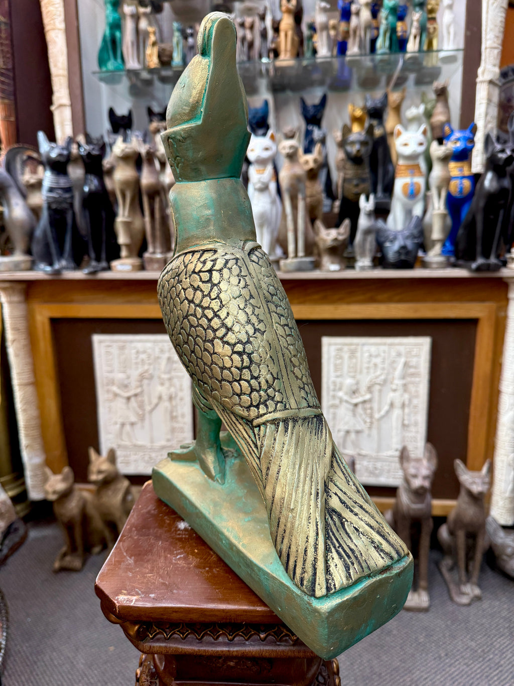Rear three-quarter view of the Horus statue showing overlapping wing feathers, a long patterned tail and the green and gold base.