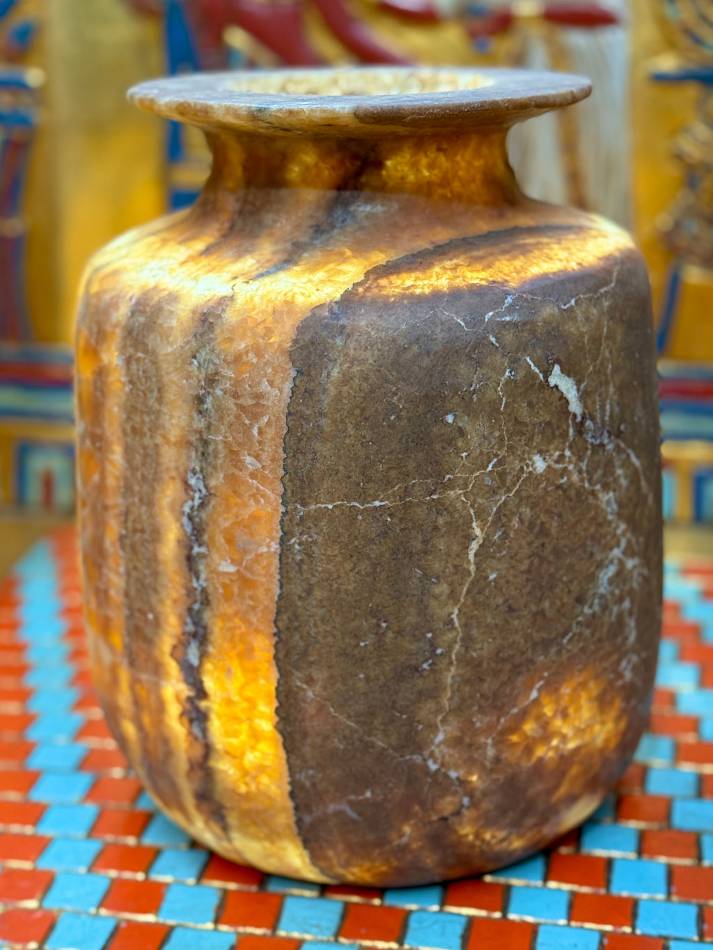 Squared alabaster vase with rounded corners, smoky brown stone, lighter vertical stripes and a flared rim — illuminated view showing amber-coloured stone.