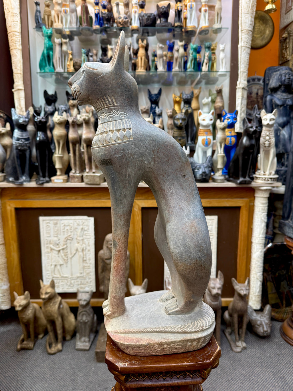 Full side view of the seated Bastet statue showing its long forelegs, curved haunches and tail along the base.