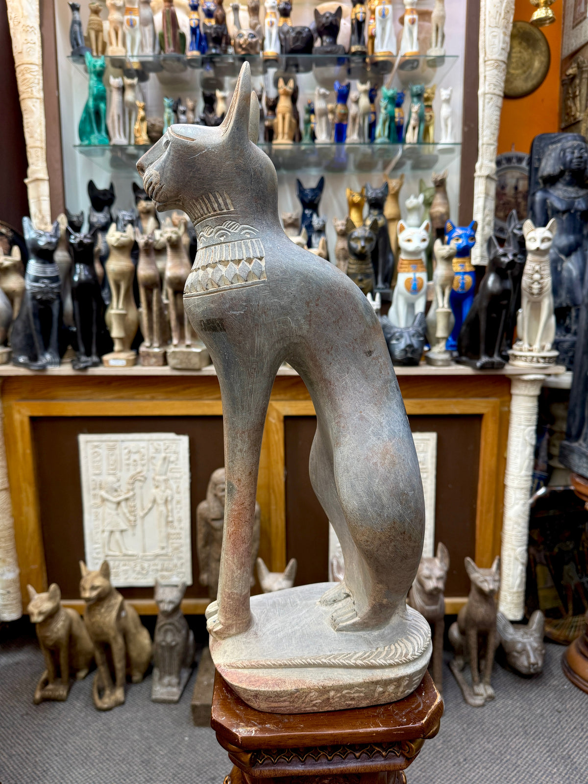 Full side view of the seated Bastet statue showing its long forelegs, curved haunches and tail along the base.