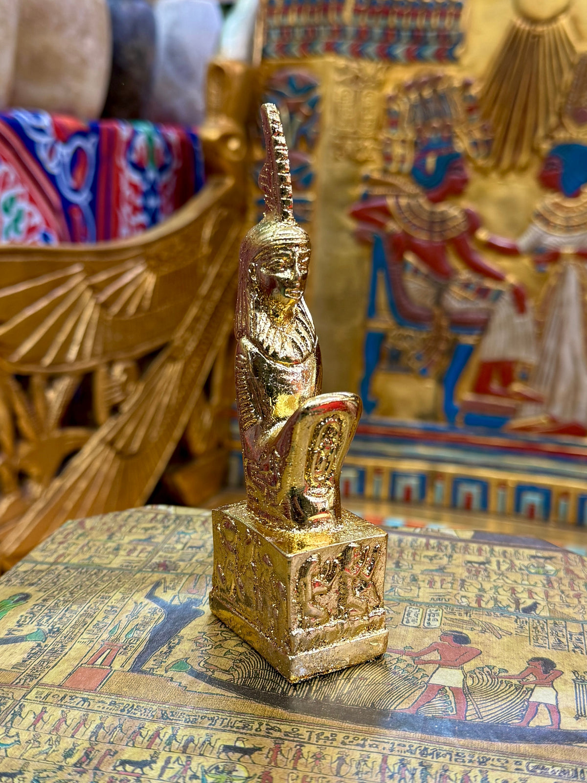 Front angled view of the gold finish Maat kneeling statue with tall feather headdress and decorated square base.