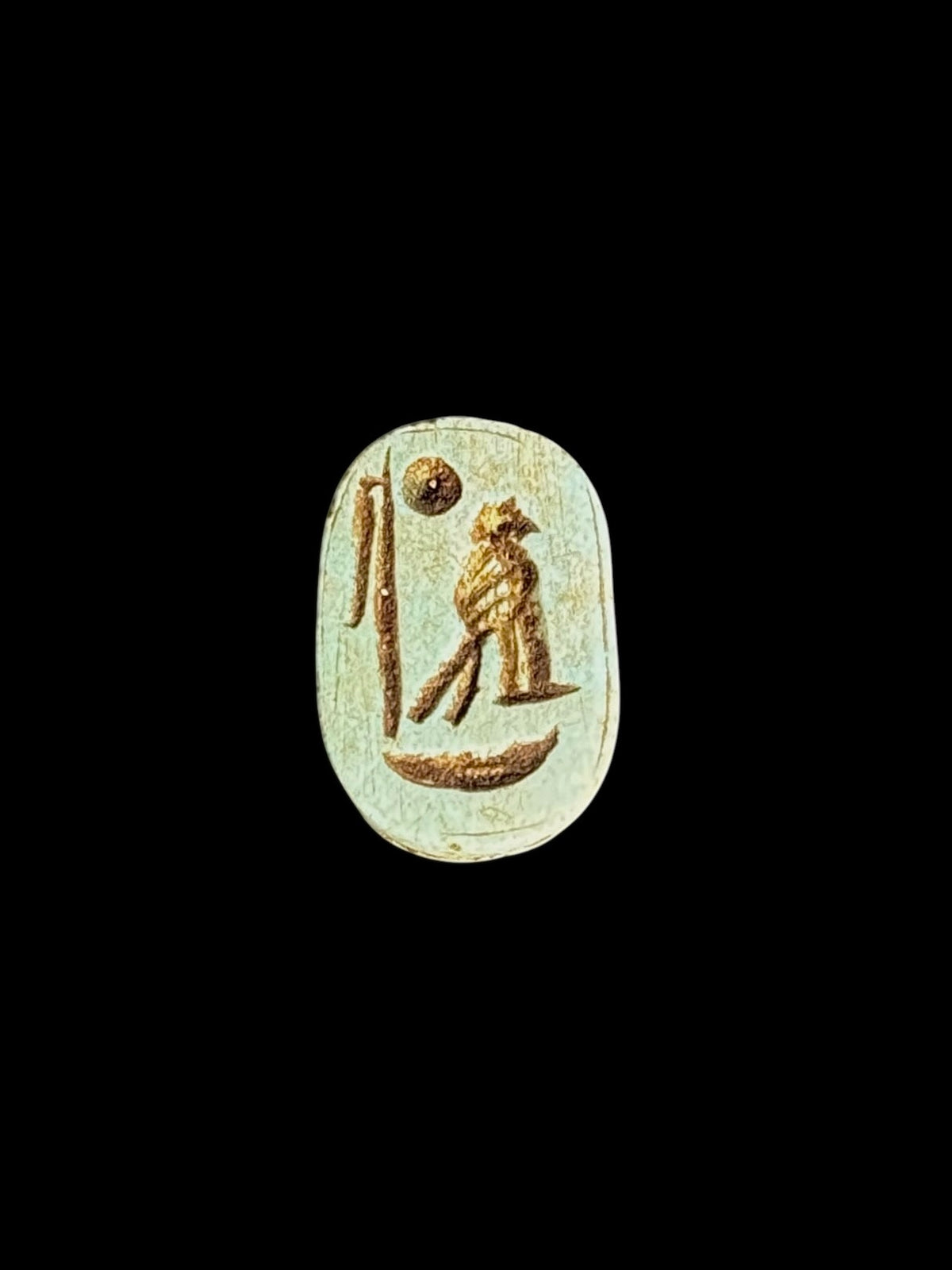Pale green oval underside of the stone scarab, showing brown incised motifs and a border against a black background.
