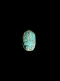 Top view of a turquoise green stone scarab with outlined wing cases and scattered brown and gold-toned areas against a black background.