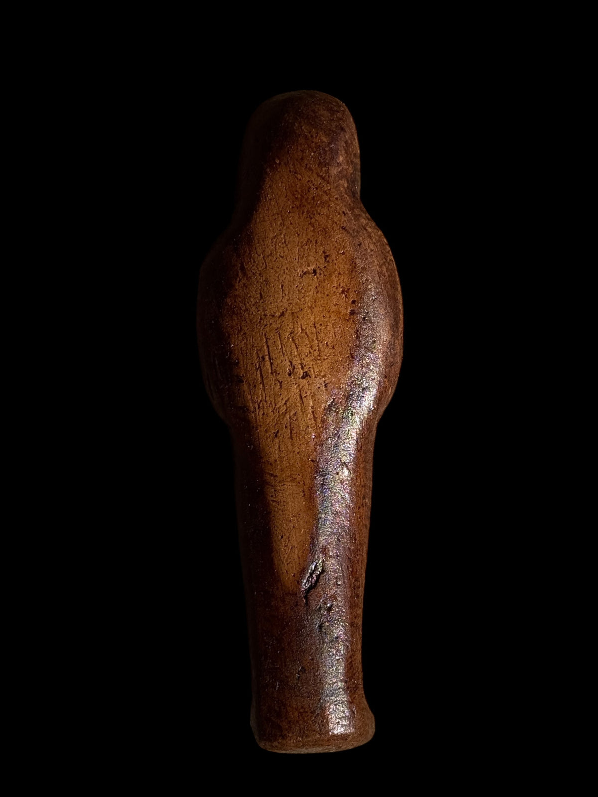 Rear view of the brown Egyptian stone figurine with winged Isis, showing its plain rounded back, textured surface and tapered lower body.