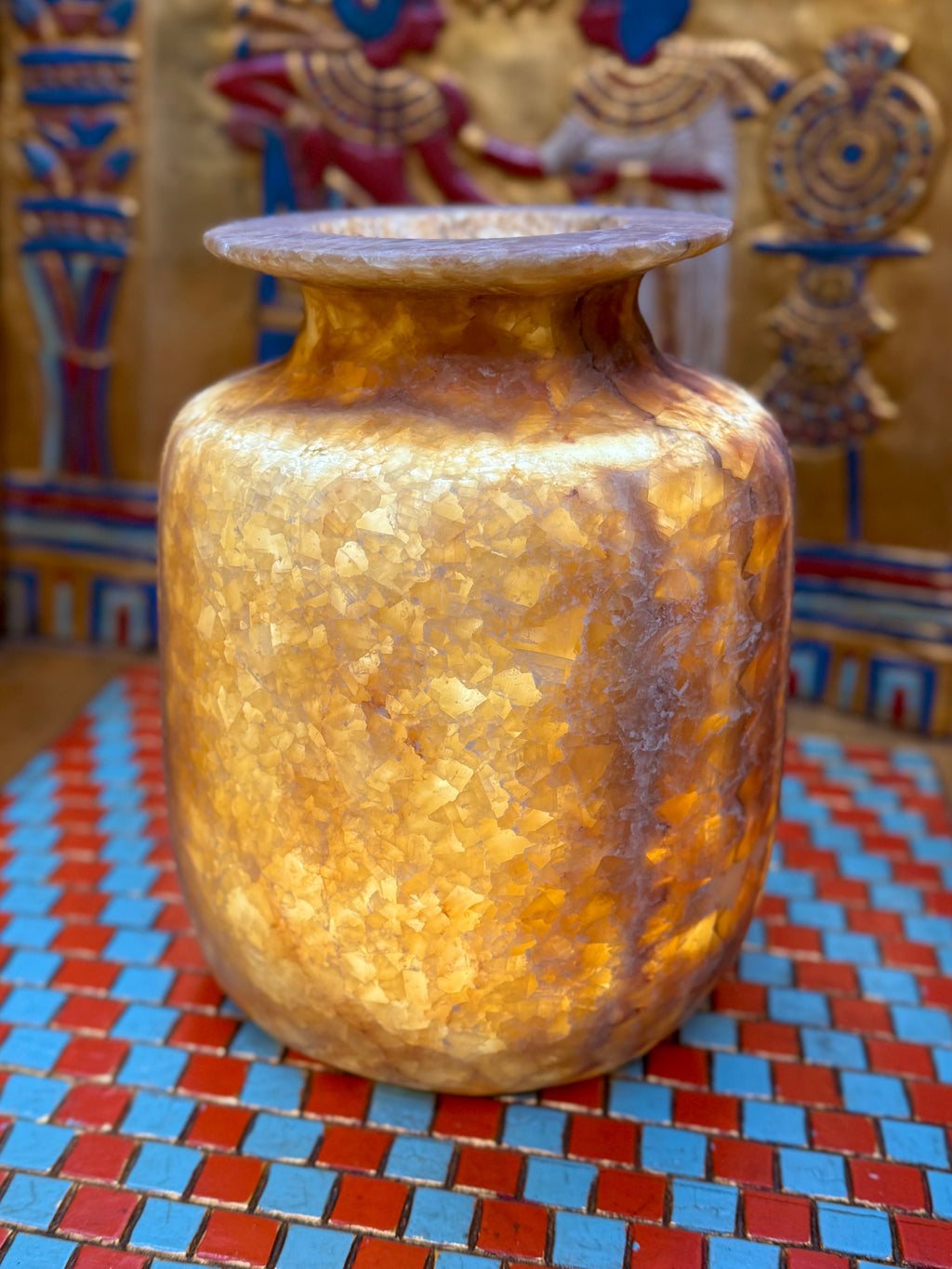 Squared alabaster vase with rounded corners, smoky brown stone, lighter vertical stripes and a flared rim — illuminated view showing amber-coloured stone.