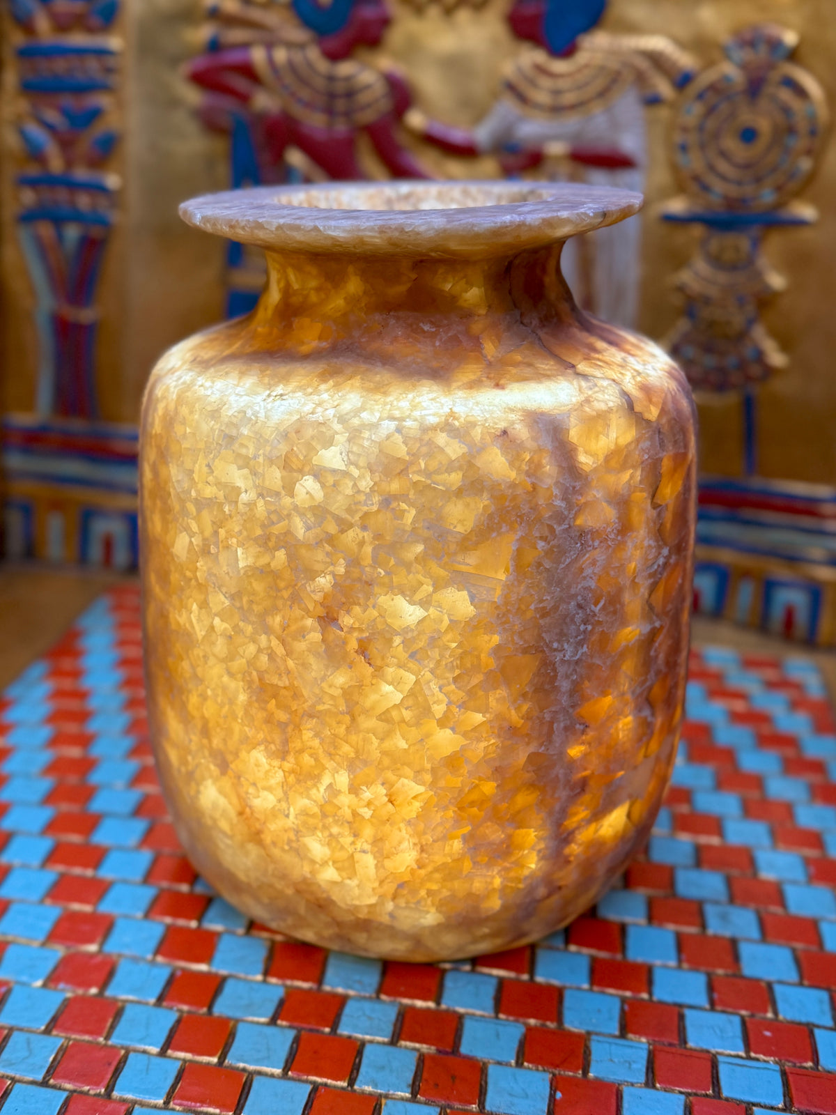 Squared alabaster vase with rounded corners, smoky brown stone, lighter vertical stripes and a flared rim — illuminated view showing amber-coloured stone.