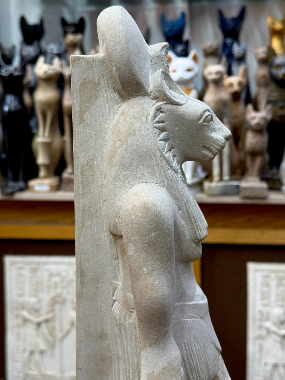 Side profile of Sekhmet statue showing the projecting lioness muzzle, sun disc, headdress and tall back pillar.