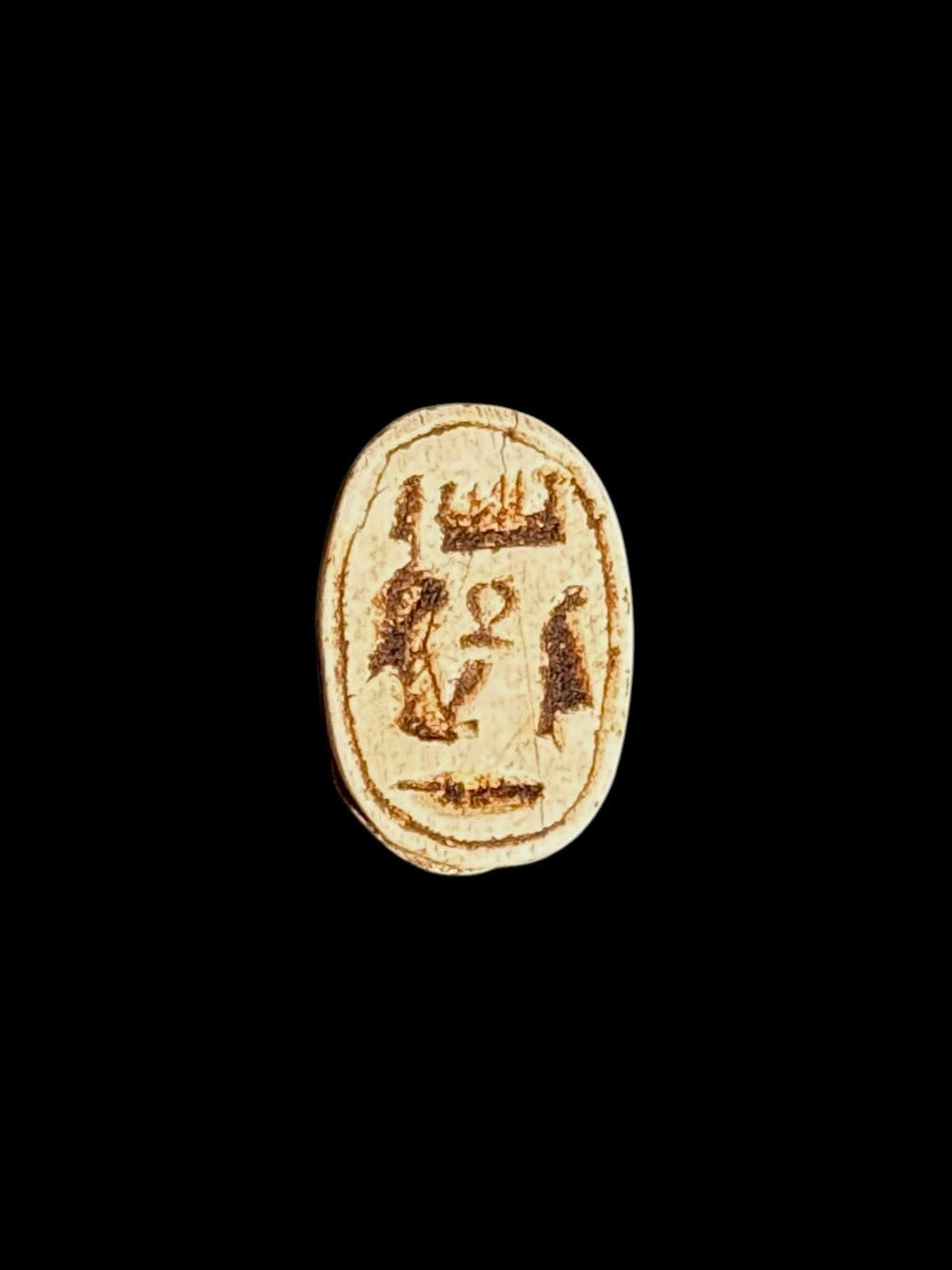 Reverse of the cream-coloured stone scarab showing brown recessed Egyptian-style symbols within an oval border.