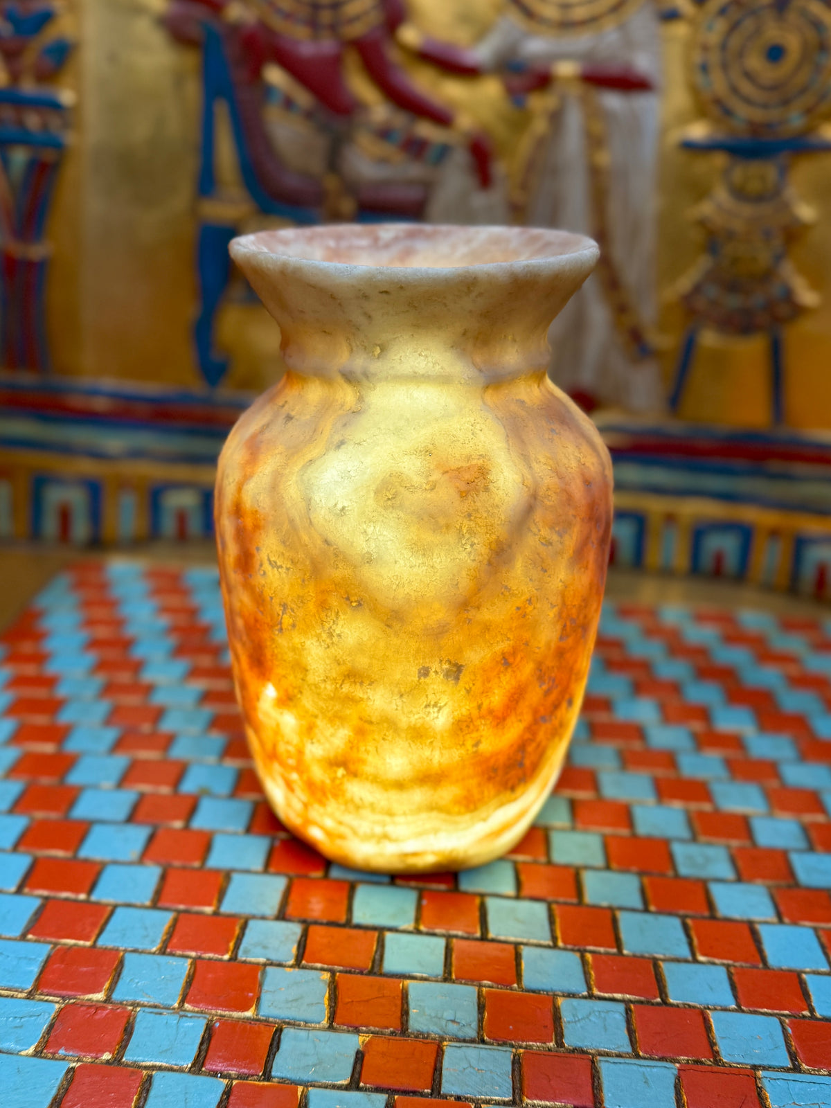 Small curved alabaster vase with cream and taupe markings and a softly flared cup-shaped rim — illuminated view.
