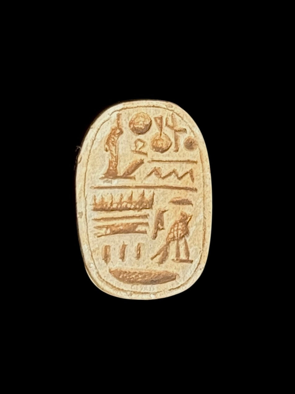 Underside of the stone scarab showing brown-toned incised symbols within an oval border against a black background.