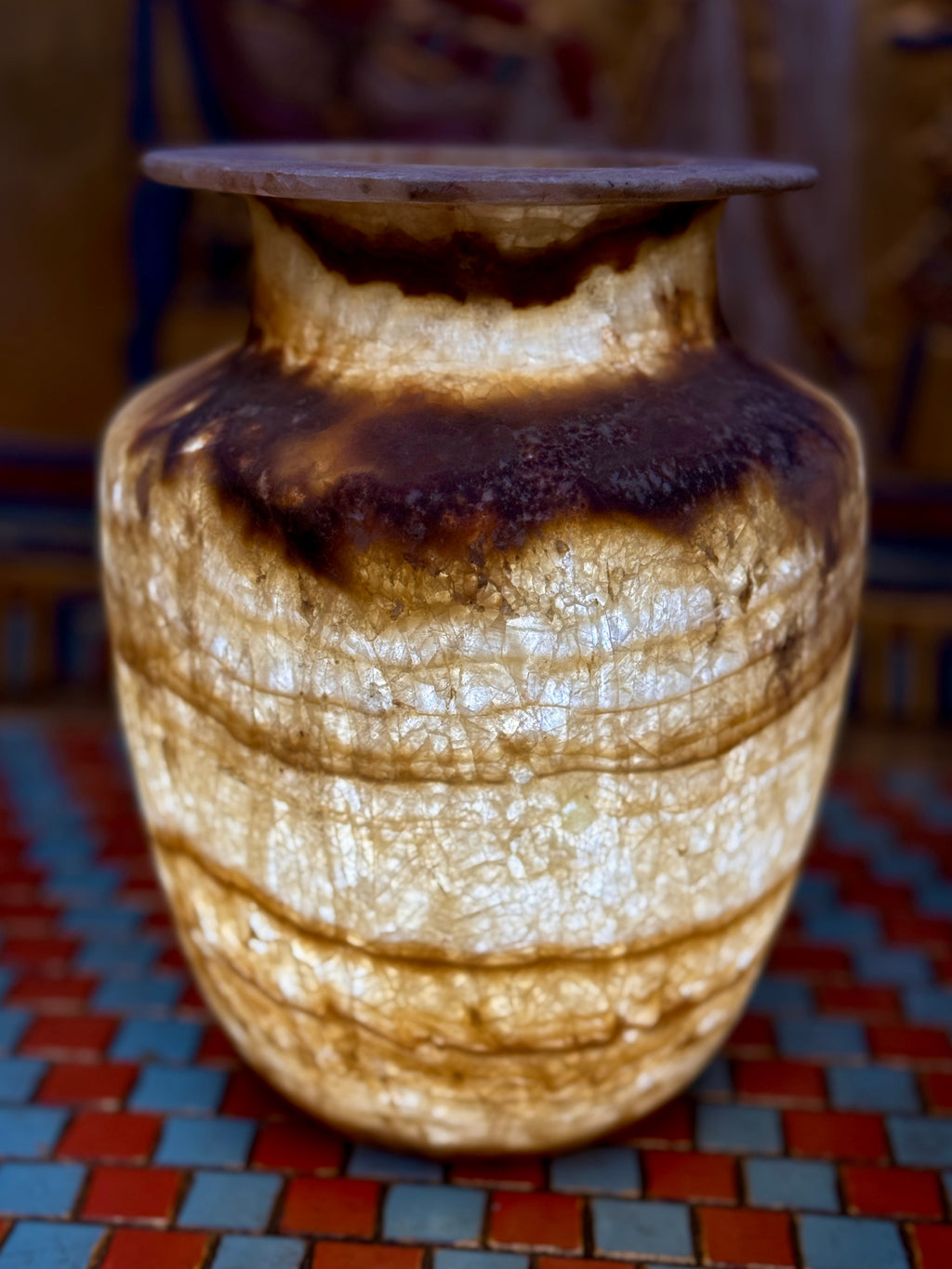 Alabaster vase with dark chestnut-coloured neck and shoulder bands, fine horizontal lines and a flared rim — illuminated view.
