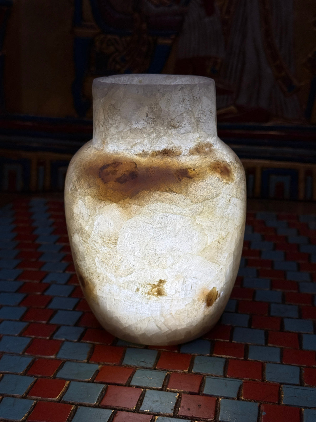 Small cream alabaster vase with a straight neck, rounded shoulders and a honey-coloured marking — illuminated view.
