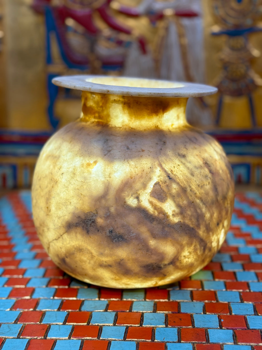 Rounded taupe and cream alabaster vase with sweeping markings, a short neck and wide flat rim — illuminated view.