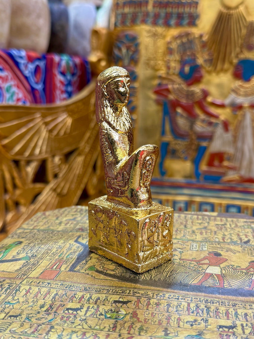 Front angled view of the gold finish Isis kneeling statue with sculpted headdress and decorated square base.