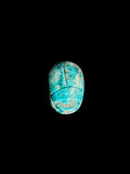 Top view of an oval turquoise-coloured scarab with incised beetle details and mottled cream and brown areas against a black background.