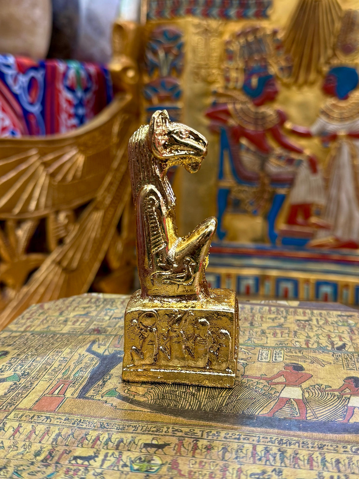 Side view of the gold finish Khnum kneeling statue with ram head, sculpted headdress and decorated square base.