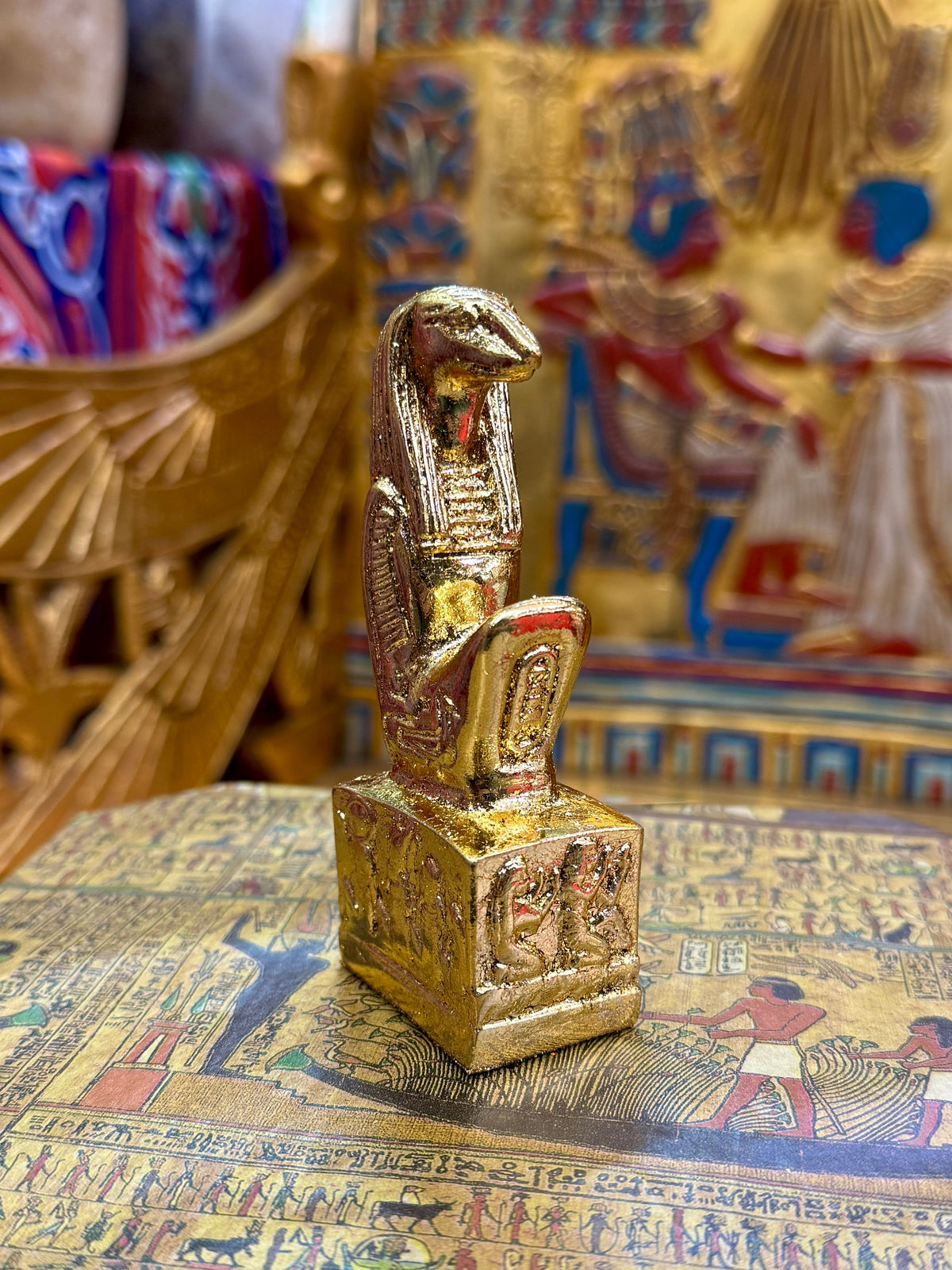 Front angled view of the gold finish Thoth kneeling statue with sculpted head, striped headdress and decorated square base.