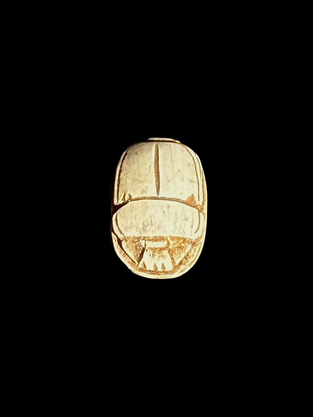 Top view of a cream-coloured stone scarab with ochre-brown lines defining the wings and beetle body against a black background.