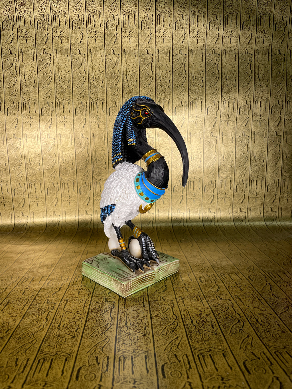 A statue of Thoth, the Egyptian god of wisdom, with an Ibis head and a blue and gold colored body standing on a green base.