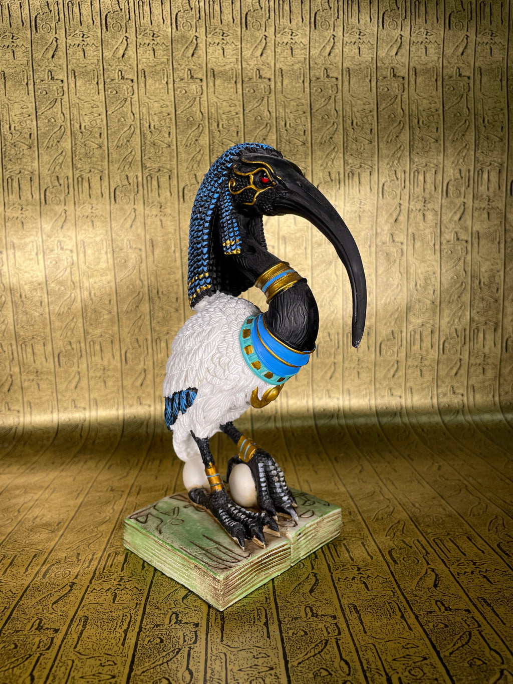 A statue of Thoth, the Egyptian god of wisdom, with an Ibis head and a blue and gold colored body standing on a green base.